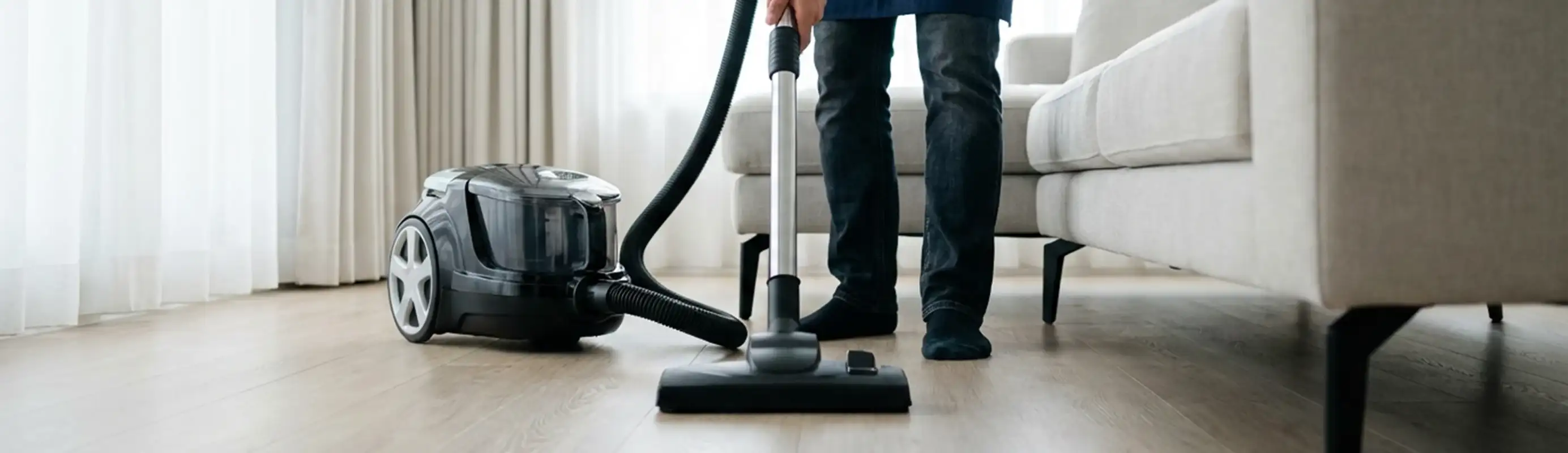 Professional house cleaner vacuuming a living room floor with a canister vacuum cleaner, Phoenix, AZ.
