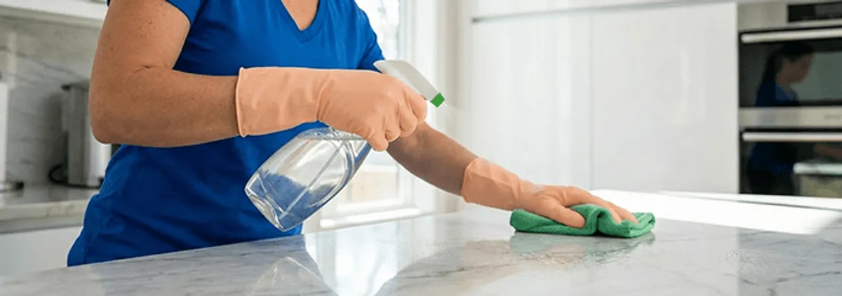 Maid service worker spraying and wiping a kitchen countertop with a microfiber cloth for sanitizing, Phoenix, AZ.
